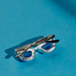 Colgante unisex con forma gafas cuya montura es de plata y las patillas están chapadas en oro negro. Las lentes son la piedra calcedonia azul. En sus bordes tiene una circonita blanca
