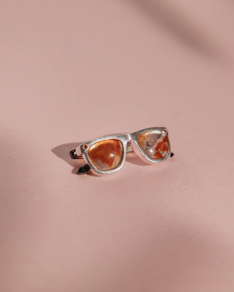 Colgante de gafas unisex con la montura de plata y chapada en oro negro. Los cristales son un cuarzo rojo con dendrítas. Tiene dos circonitas naranjas en los laterales.